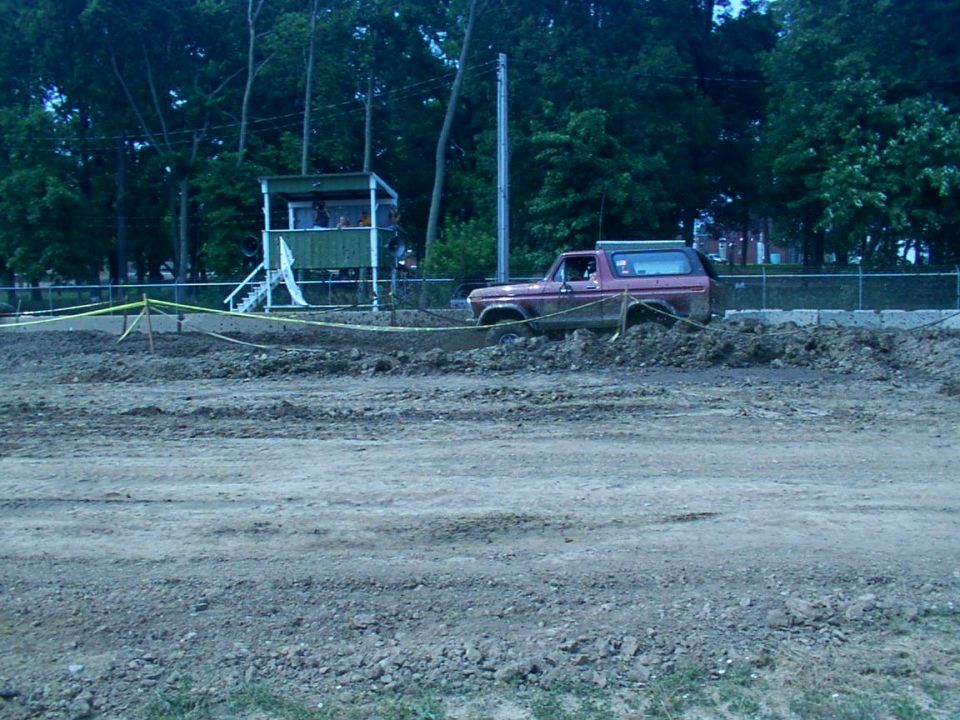Red 1978 Ford Bronco stuck in a muddy track with a green observation booth in the background