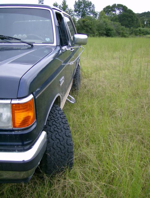 1990 Ford Bronco - A dark blue Ford Bronco is parked in a grassy field, viewed from the front quarter panel.