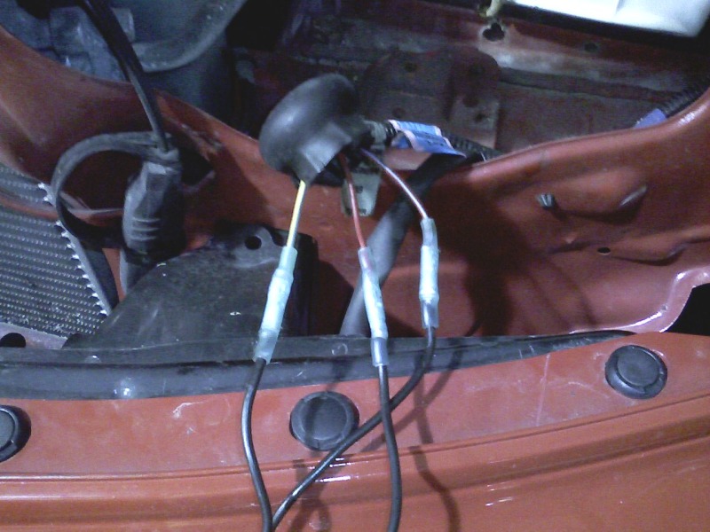 Three wires with clear crimp connectors spliced through a rubber grommet at the cowl of an orange vehicle