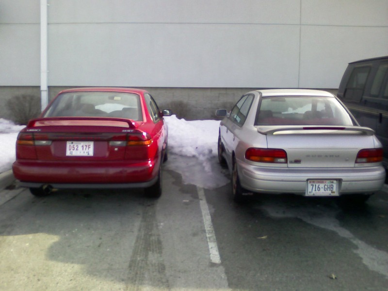 Rear view of red Subaru Legacy sedan parked beside silver Subaru Impreza in snowy lot
