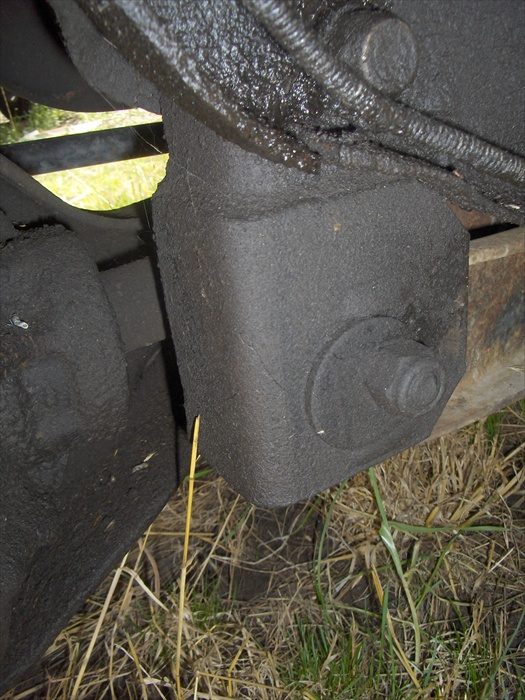 Close-up of black-painted undercarriage bracket with large bolt on a Ford F-150, grass below