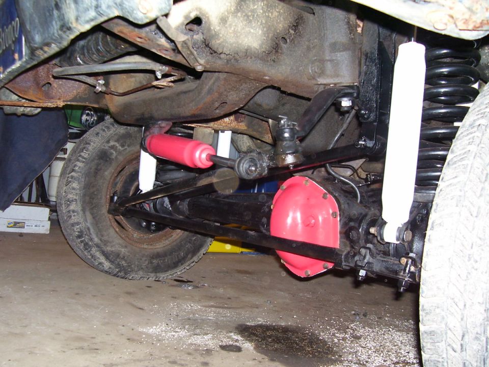 Front axle and suspension under a Ford Bronco showing red diff cover, coil springs, and shocks