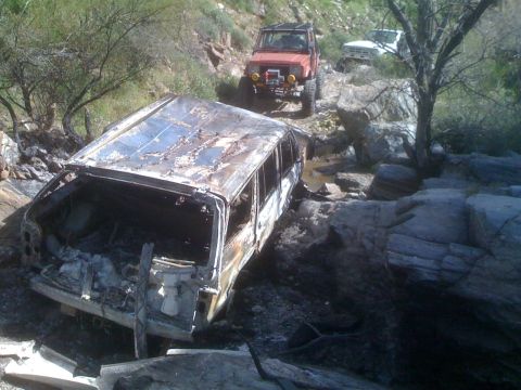 1966 Ford Bronco - A severely damaged vehicle lies on a rocky trail, with two other off-road vehicles navigating the difficult terrain behind it.