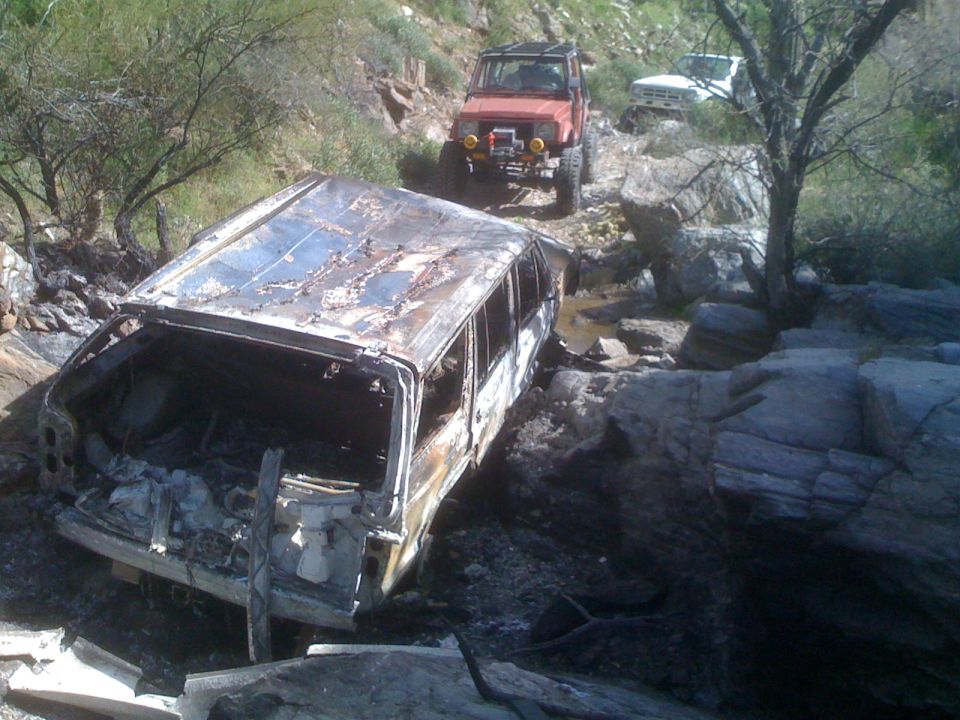 Burnt-out SUV on rocky trail with two other off-road vehicles behind it