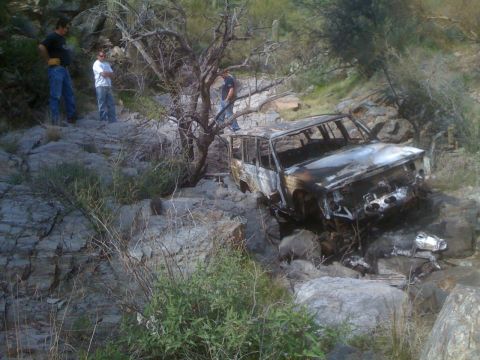 1966 Ford Bronco - A severely damaged SUV sits in a rocky, off-road environment, with three people observing the scene.