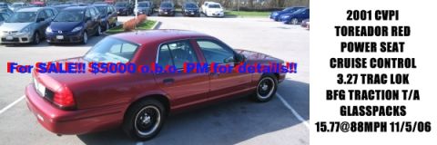 2001 Ford Crown Victoria - A red sedan is parked in a lot with other vehicles, advertised for sale with its specifications listed.