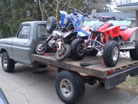 1979 Ford F-150 - Flatbed Ford F-150 truck transports ATVs and a dirt bike on its wooden deck.