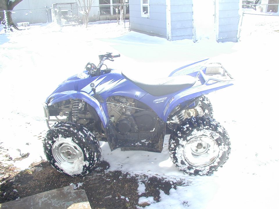 Blue Yamaha ATV quad parked on snowy ground beside a house
