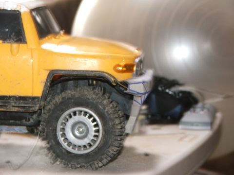 1996 Ford Bronco - A close-up of a yellow toy SUV's front corner, showing its tire and a detailed bumper.