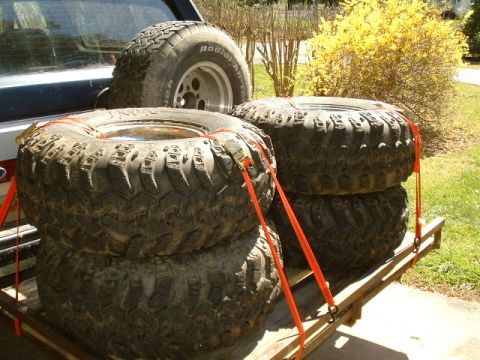 1991 Ford Bronco - Several off-road tires are secured with orange straps on a wooden trailer.