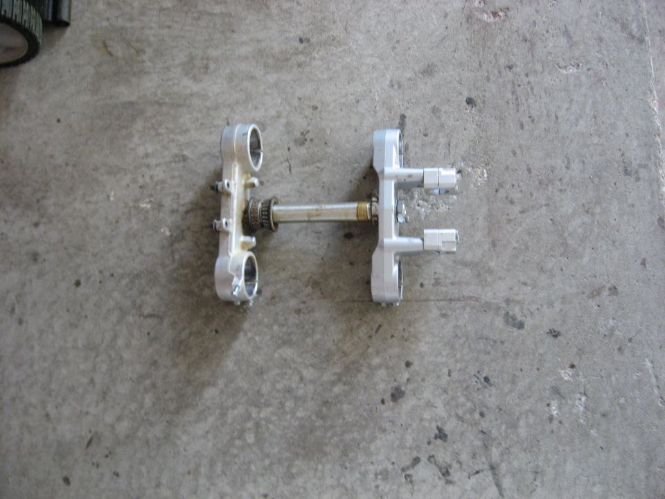 Aluminum motorcycle triple clamps and steering stem laid on a concrete garage floor