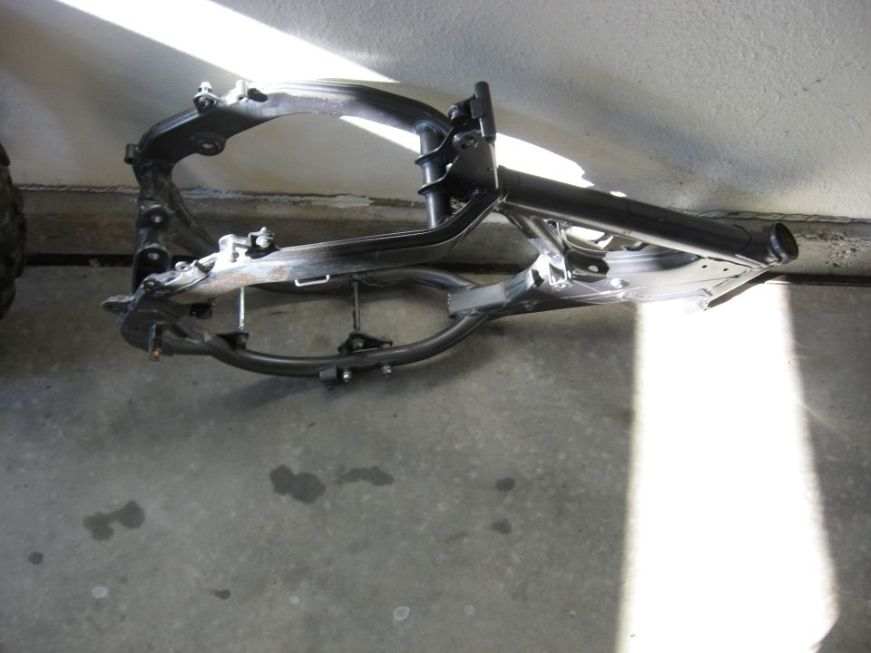 Stripped dirt bike frame with aluminum beams and black steering head on a garage floor