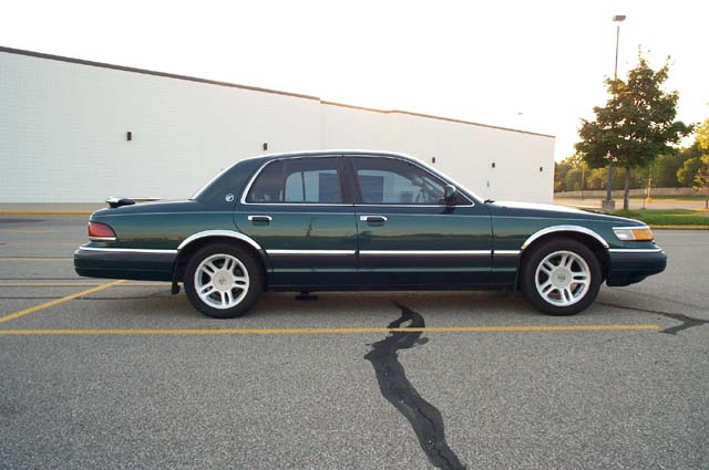 Driver-side profile of green Mercury Grand Marquis sedan beside a blank building