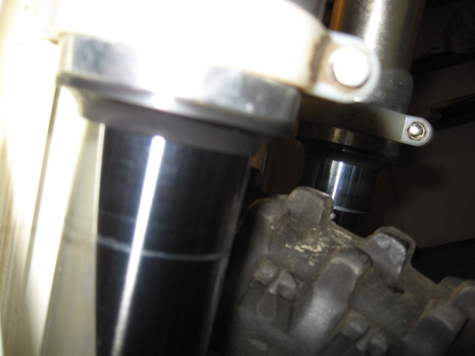 Close-up of dirt bike front forks with black lower tubes and knobby tire below