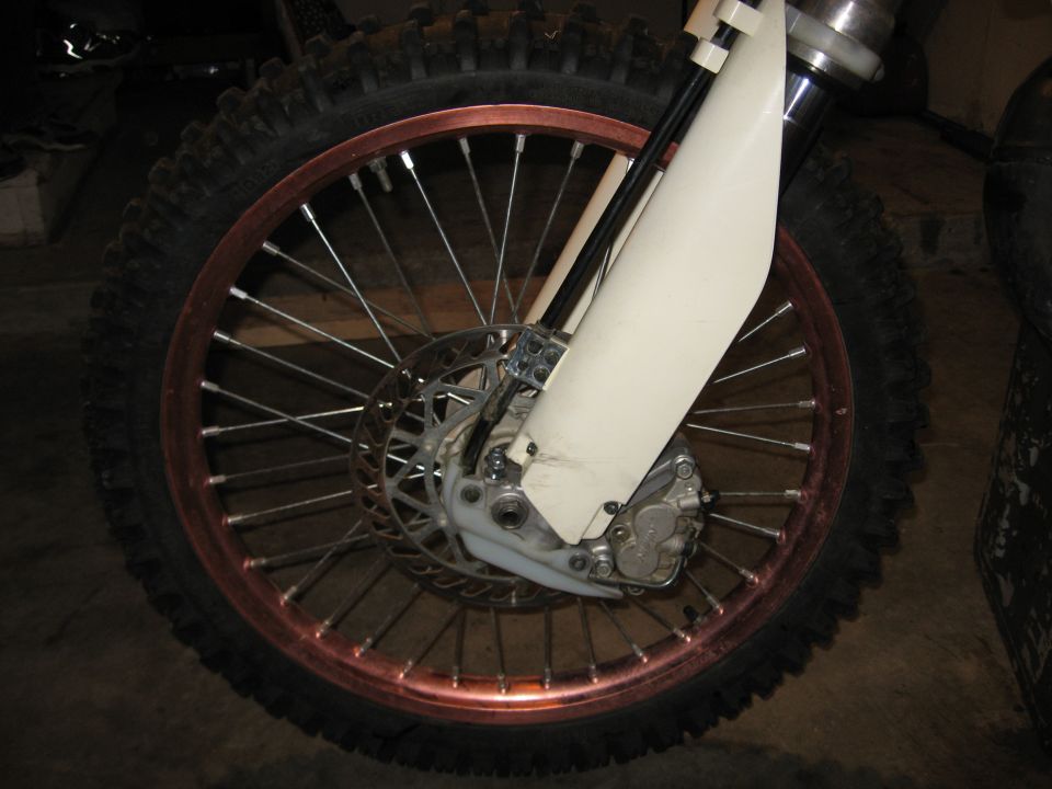 Motorcycle front wheel with copper rim, knobby tire, disc brake, and white fender