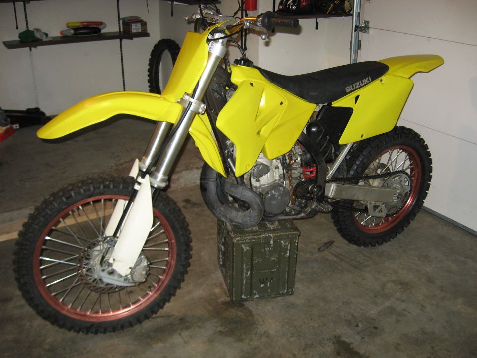 Yellow Suzuki motocross dirt bike in a garage with front wheel on an ammo can