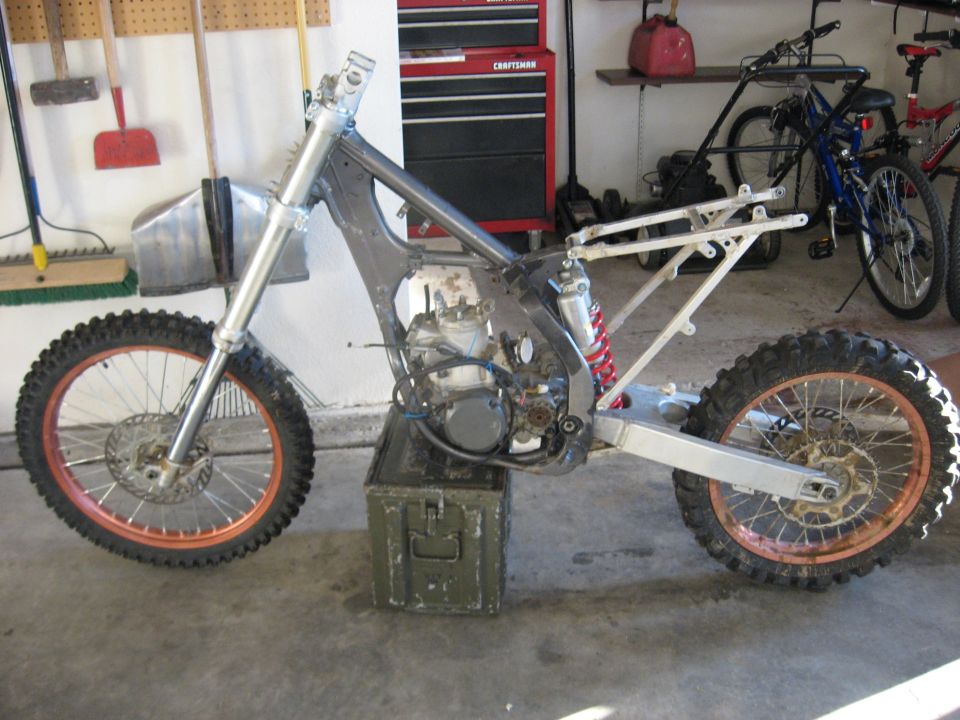Partially assembled dirt bike frame and engine resting on an ammo box in a garage