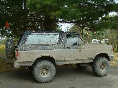 1991 Ford Bronco - This 1991 Ford Bronco is covered in mud, showing its side profile and rear-mounted spare tire.
