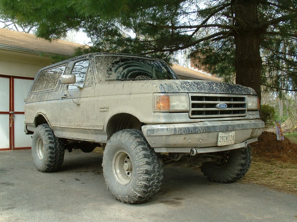 Mud-covered 1991 Ford Bronco with large off-road tires parked outside a garage