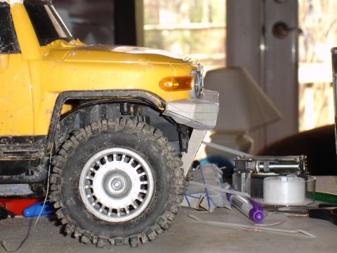 1996 Ford Bronco - A close-up of a yellow toy truck's front wheel and bumper area, set against a backdrop of indoor clutter.