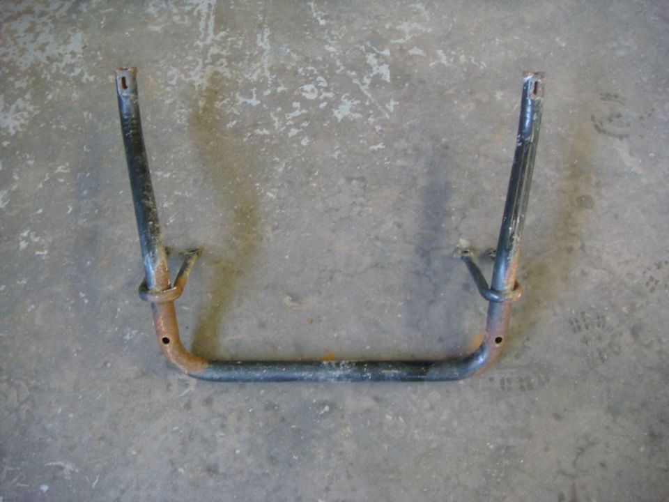 Dark metal tubular bracket with rust and bolt holes on concrete