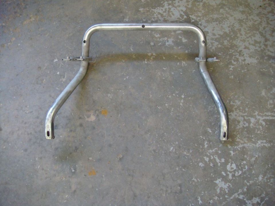 Stripped bare-metal tubular roll bar with mounting brackets, lying on a concrete garage floor