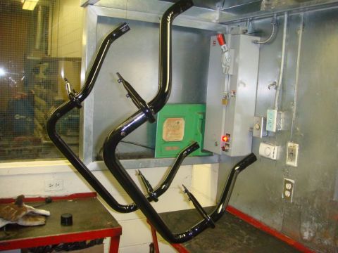1996 Ford Bronco - Freshly powder-coated gloss black roll bar tubes and support legs hanging on wire in a shop next to a gray electrical disconnect panel and…