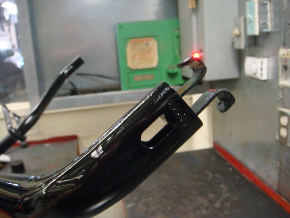 Freshly coated glossy black steel bracket hanging in an industrial paint booth