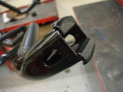 1996 Ford Bronco - Freshly painted glossy black stamped-steel bracket held up in a shop, with a raised cast part number, a keyhole-shaped slot and a rounded l…