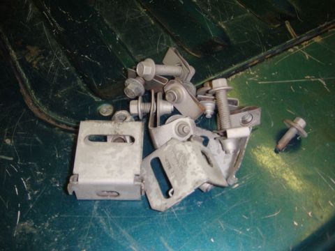 1996 Ford Bronco - A pile of zinc-plated stamped steel mounting brackets and flange-head bolts, one bracket cast with a Ford oval part marking, laid out on a…