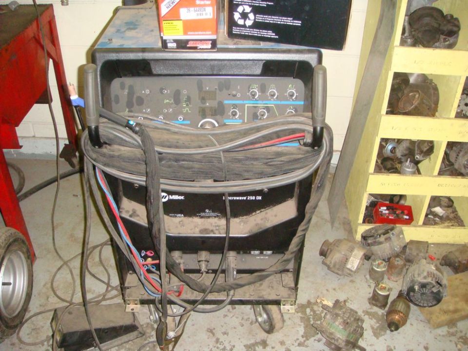 Miller "Diversion 250 DX" welder on casters, with assorted car alternators and parts on shelves and floor