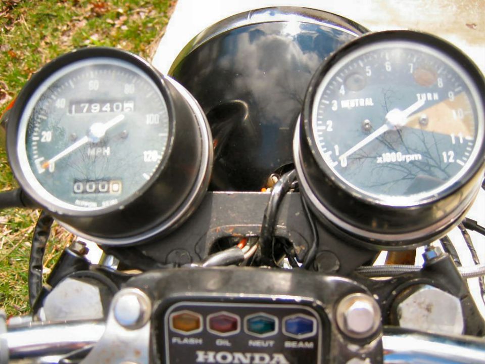 Motorcycle dashboard with speedometer, tachometer, and indicator lights. Reads HONDA