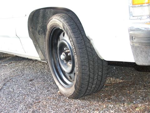 1985 Ford Crown Victoria LTD - Close-up of a white car's wheel a steel rim and "TOURING SLC" tire branding.