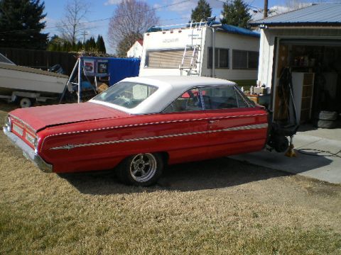 1964 Ford Galaxie - A red two-door hardtop car with a white roof is parked in a grassy yard next to a garage and an RV.