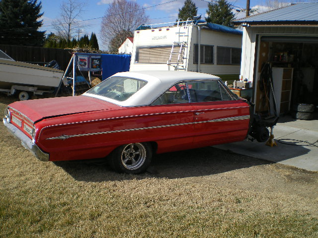 red two-door hardtop car with white roof, parked on grass next to a garage and RV