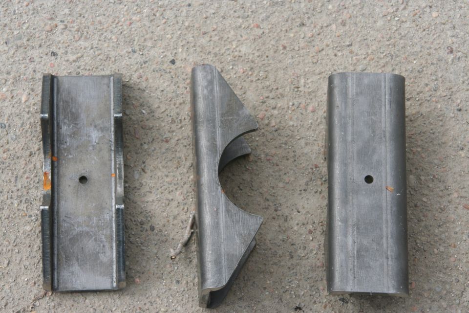 Three metal parts, one with a curved cutout, on concrete