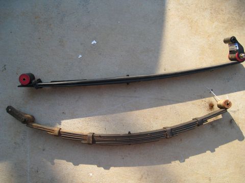 1996 Ford Bronco - Comparison of a new leaf spring with red bushings next to an older, rusted leaf spring.
