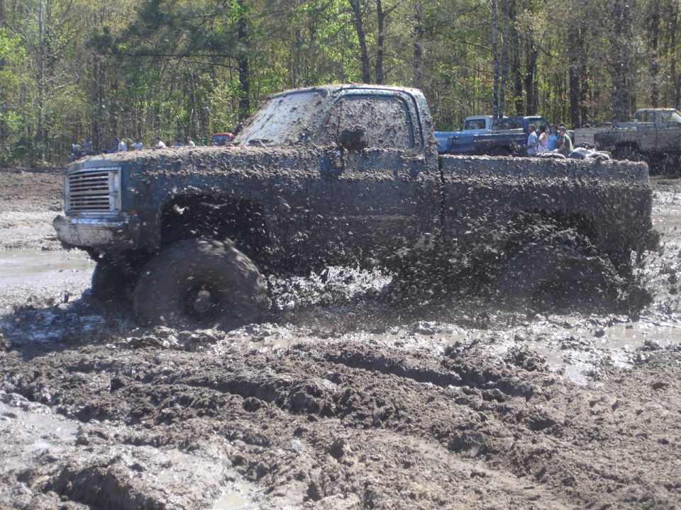 Mud-covered pickup truck stuck in mud, with other vehicles in background