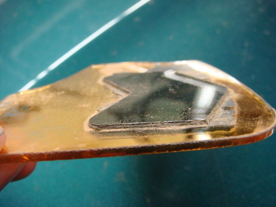 Gold-colored signal mirror part with a black inset and visible dust
