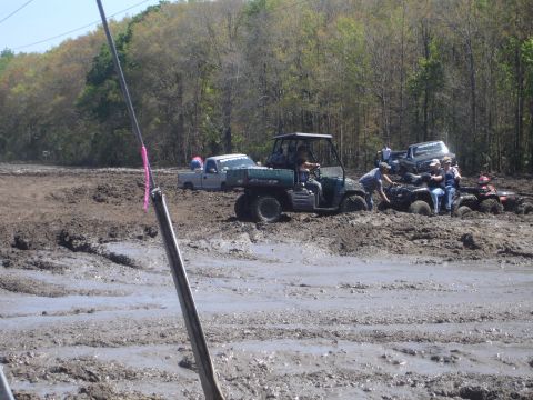 1989 Ford Bronco - Several off-road vehicles, including ATVs and a pickup truck, are stuck in a muddy terrain with people attempting to free them.