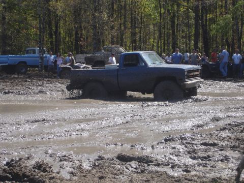 1989 Ford Bronco - A blue pickup truck is stuck in a muddy area with several people observing the scene.