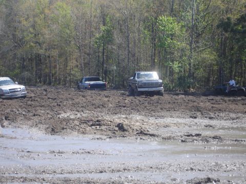 1989 Ford Bronco - Several vehicles are stuck in deep mud during an off-road event.