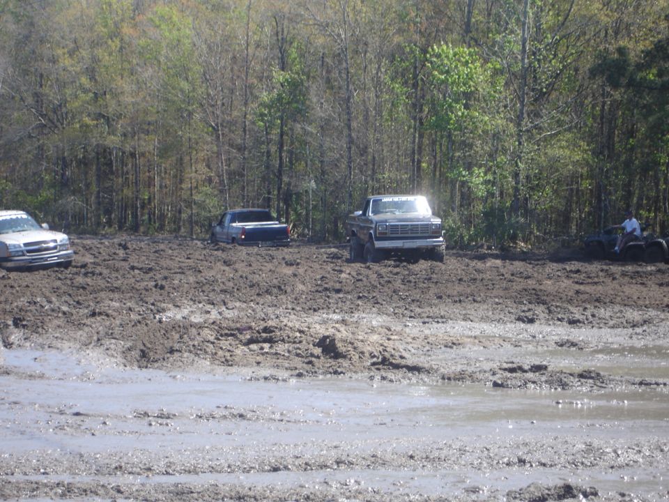 Gray pickup truck stuck in mud, with other vehicles in background