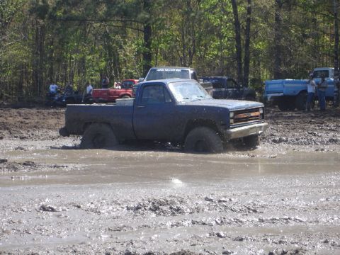 1989 Ford Bronco - Several vehicles are participating in a mud bogging event, with one truck deeply submerged in the mire.