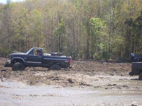1989 Ford Bronco - A black pickup truck is stuck in a muddy area with trees in the background.