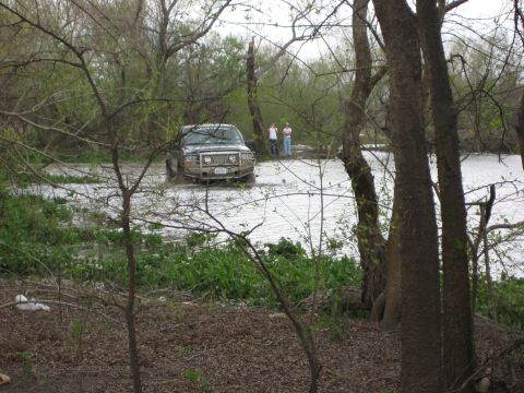 1996 Ford Bronco - A 1996 Ford Bronco navigates through a flooded area, with two onlookers observing from the bank.