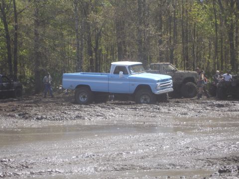 1989 Ford Bronco - A light blue pickup truck with a white roof is seen in a muddy off-road environment with other vehicles present.