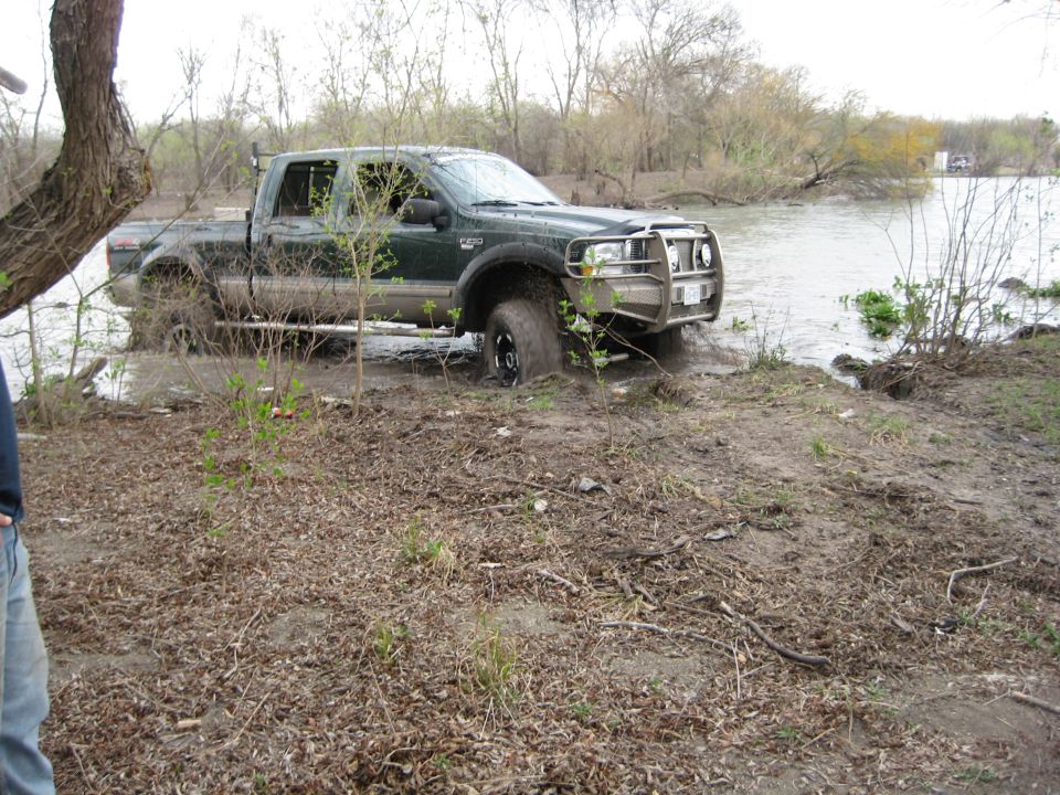 Green crew cab pickup truck with brush guard stuck in muddy water