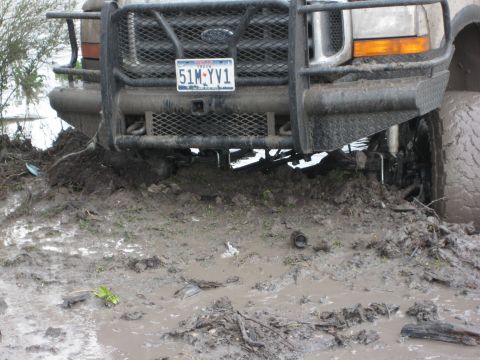 1996 Ford Bronco - A Ford truck is stuck in deep mud, with its front tires partially submerged and the chassis low to the ground.