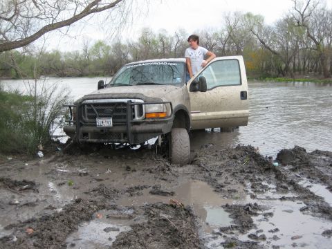 1996 Ford Bronco - A tan Ford F-250 Super Duty is stuck in mud and water, with a person standing in the open driver's door.